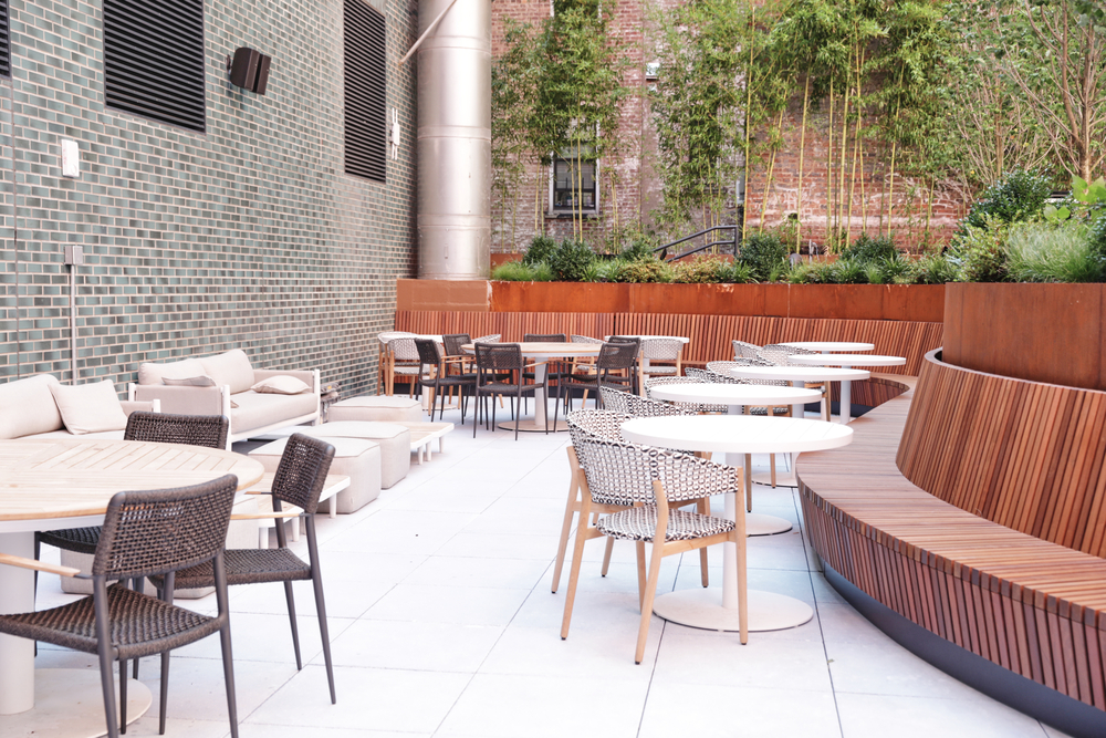 A modern outdoor seating area with a curved wooden bench, tables, and chairs.