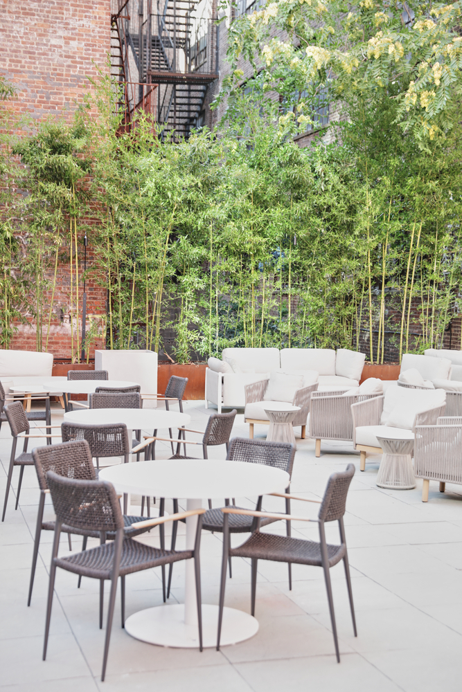 A seating area with tables and chairs, sofas, and plants in front of a brick wall.