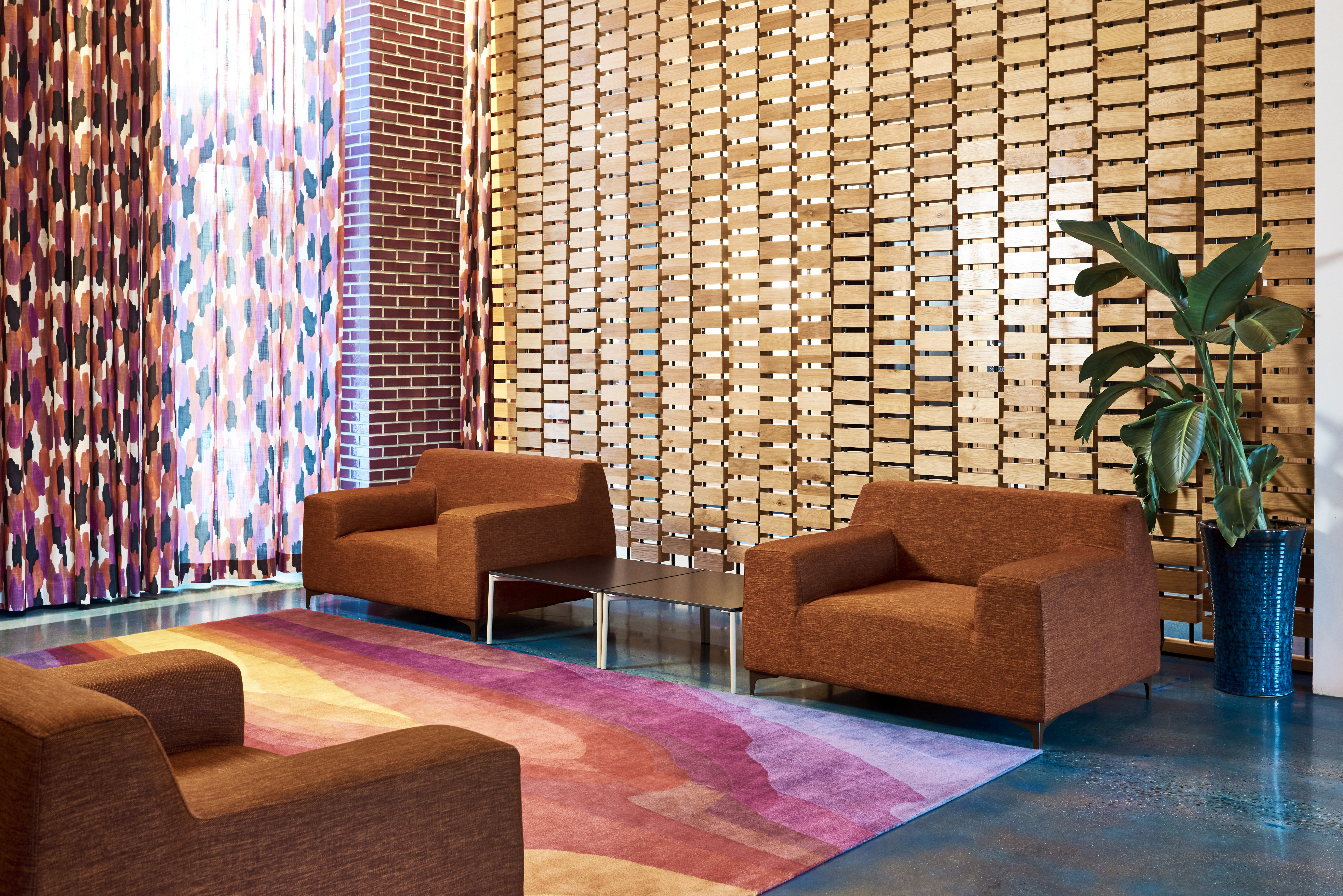 A lobby seating area with brown armchairs, a colorful rug, and abstract art on the walls.