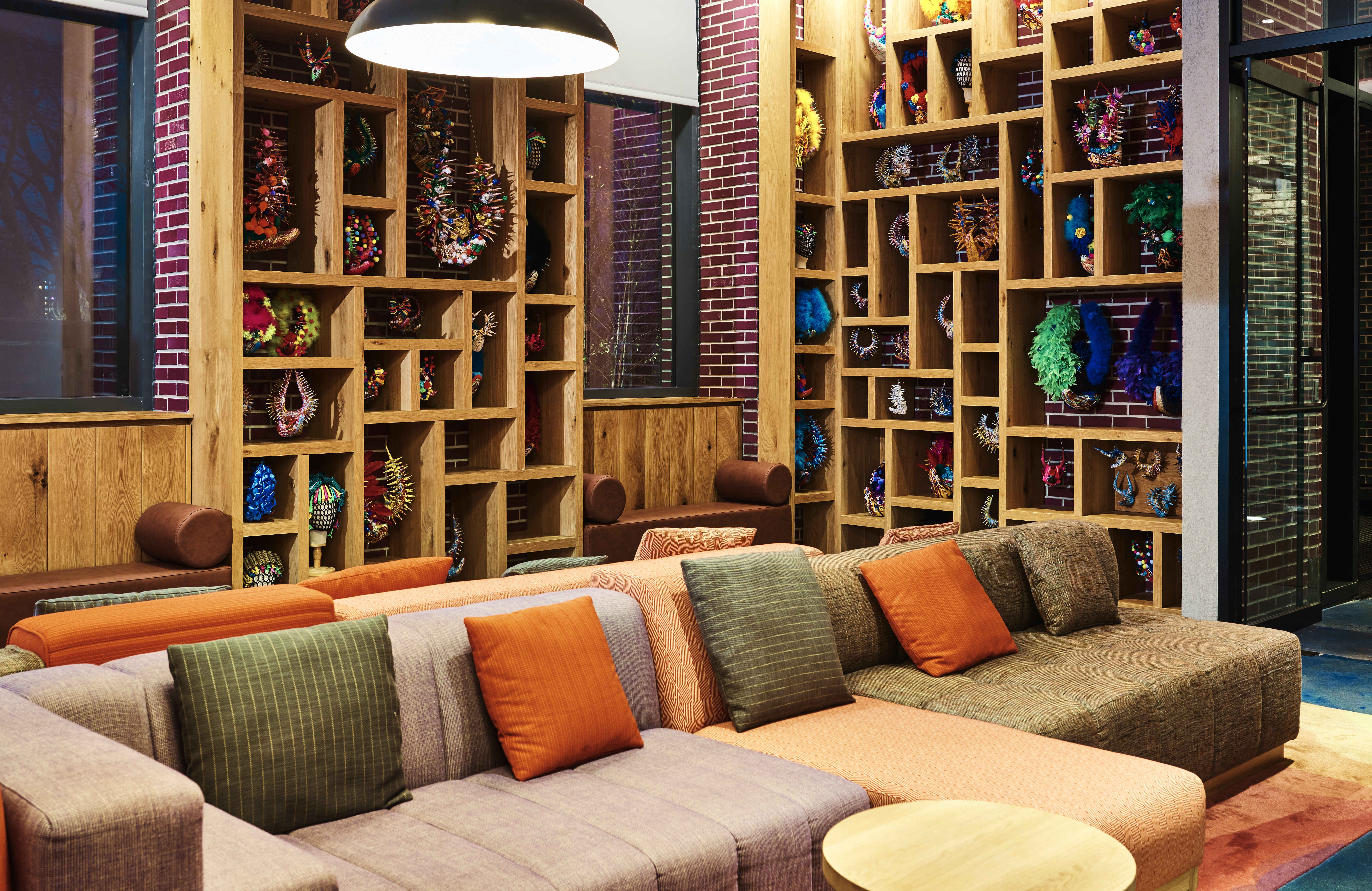 A lobby with a large sectional sofa, a coffee table, and a bookshelf filled with colorful objects.