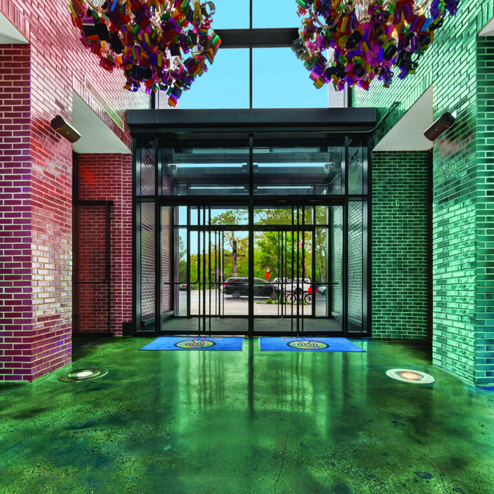 A colorful entrance with red and green brick walls, a glass door, and a chandelier.