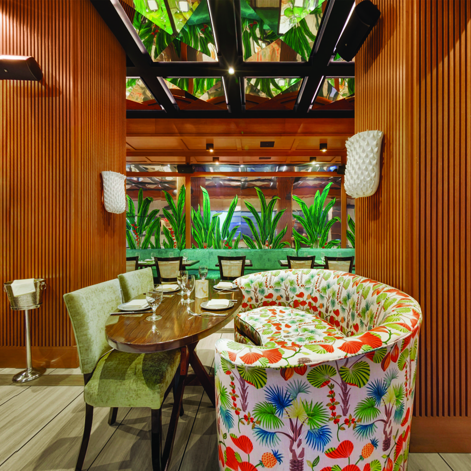 A dining area with a wooden table and chairs, a floral couch, and plants in the background.