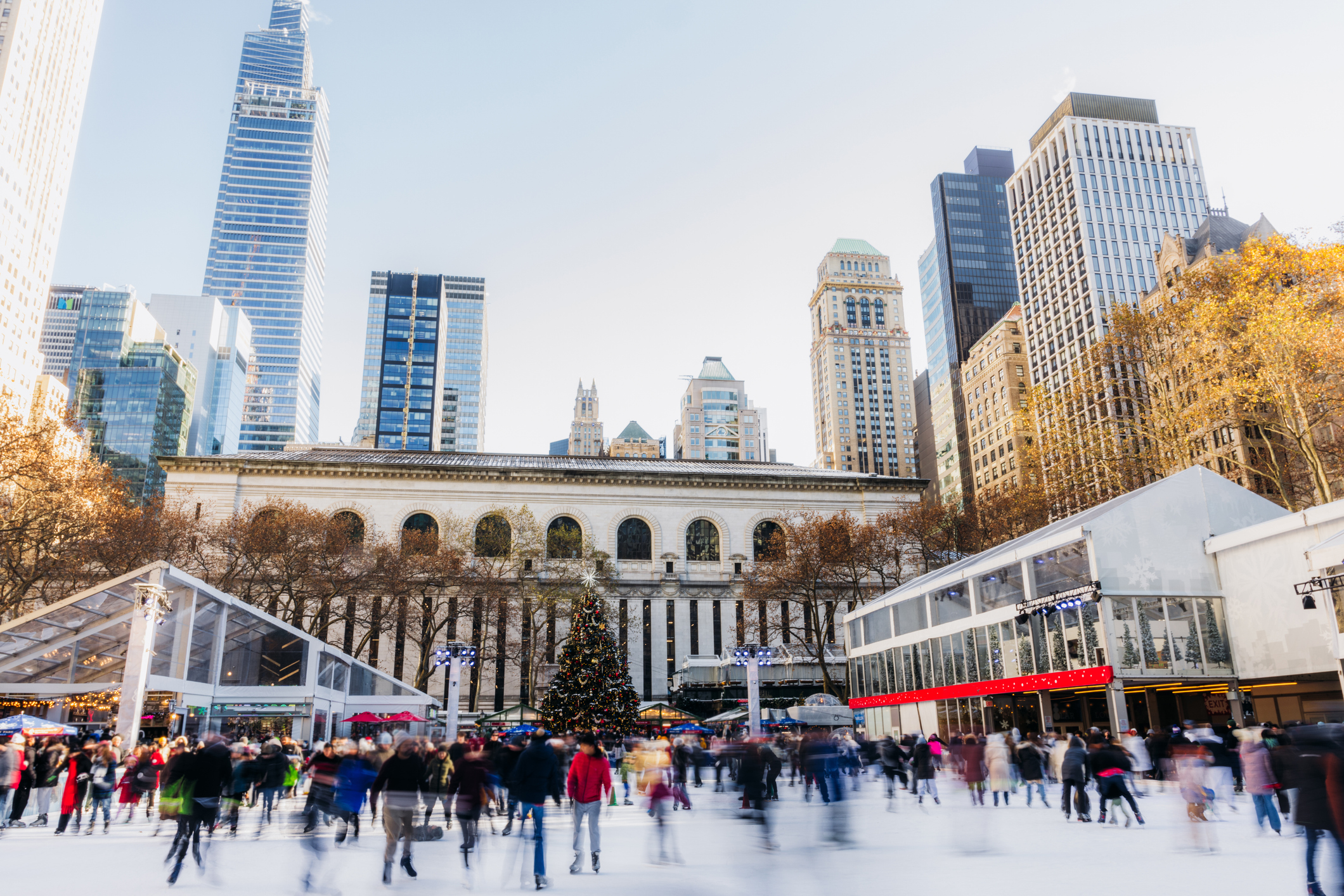 People ice skating at a rink in front of the New York Public Library, with a Christmas tree and tall buildings in the background of NYC holiday accommodations.