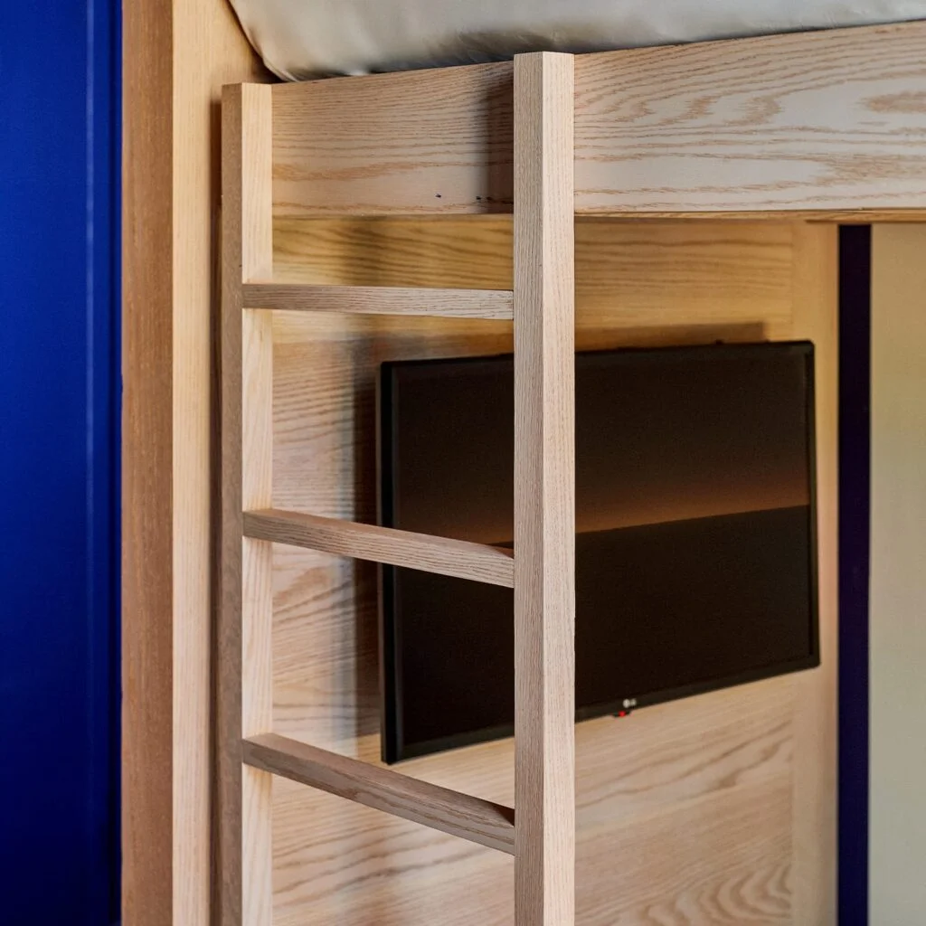A close-up of a wooden bunk bed with a black TV screen mounted on the side.
