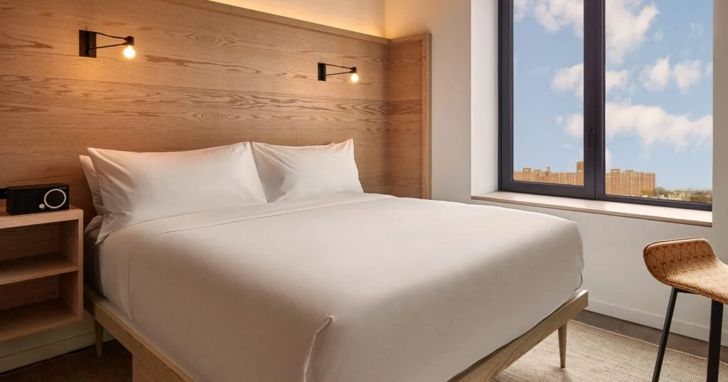 A hotel room with a large bed, wooden headboard, and city view.