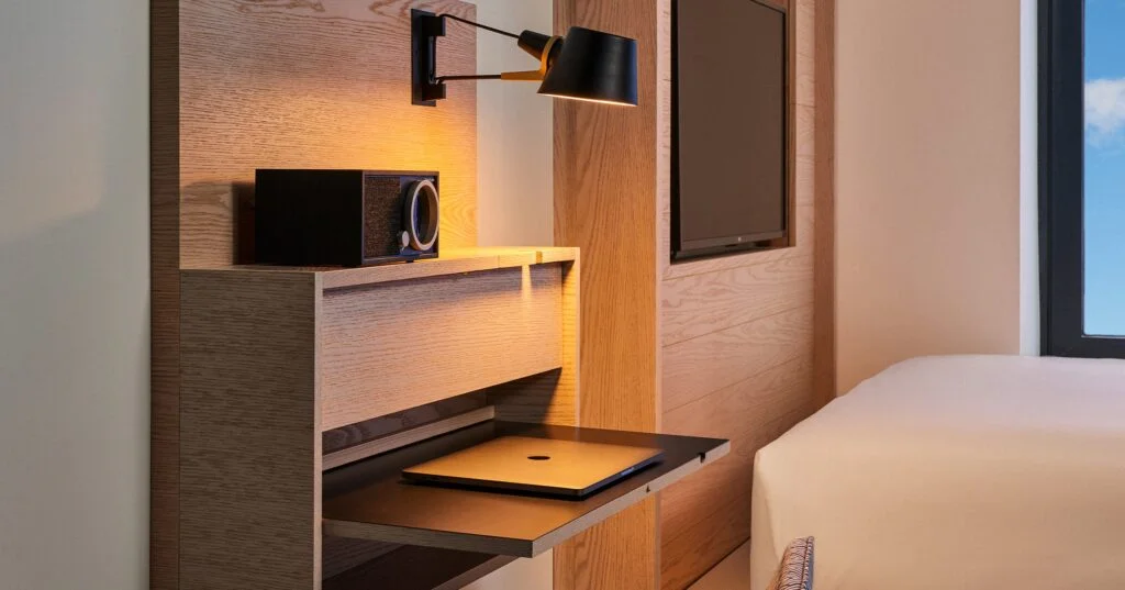 A hotel room with a bed, a desk with a laptop, a television, and a lamp.