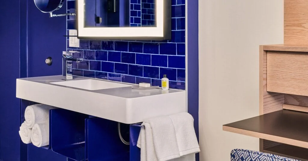 A modern bathroom sink with blue tiles, a white countertop, and a mirror.