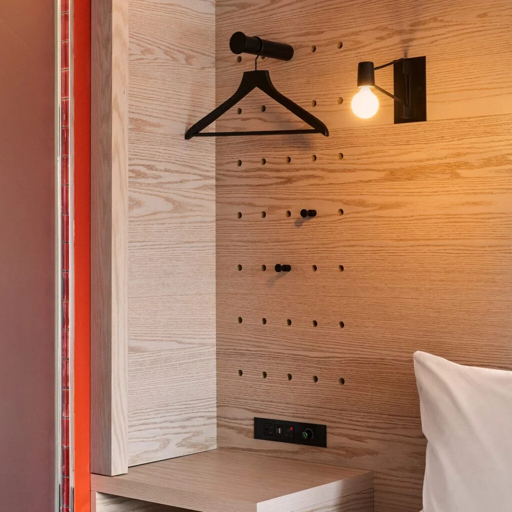 A wooden wall with a black hanger, light fixture, and electrical outlet in a room.