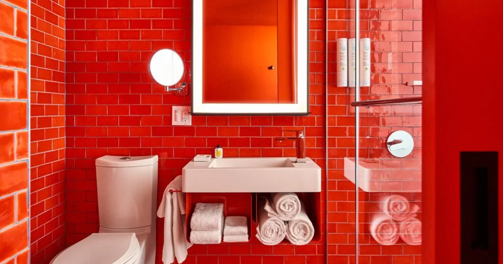 A red-tiled bathroom with a white sink, toilet, and towels.